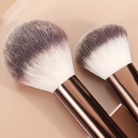 Close-up of two Briselle fluffy makeup brushes with rose gold handles on beige background
