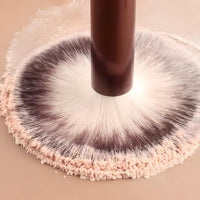 Briselle makeup brush with soft bristles dipped in loose face powder close-up