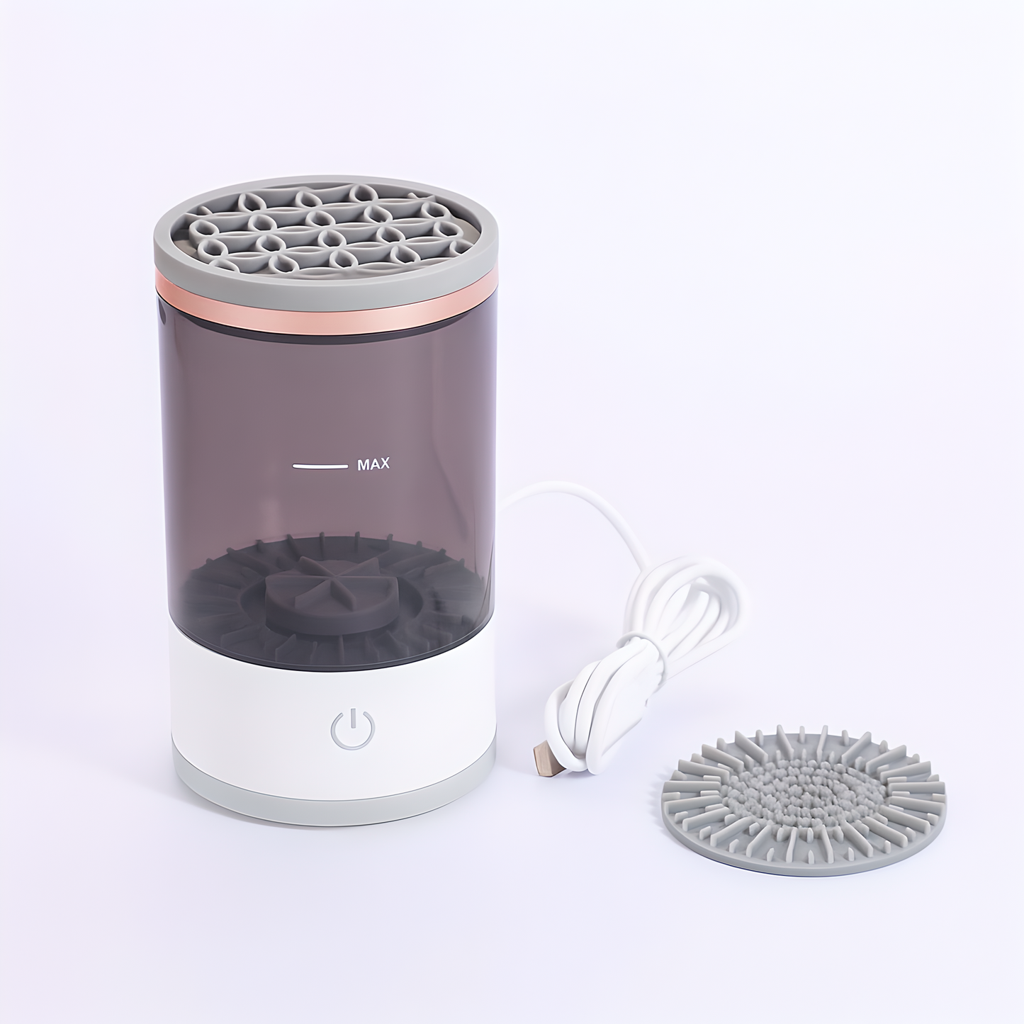 Electric automatic makeup brush cleaner with a detachable transparent rinse tank, gray silicone lid, and included USB charging cable, displayed on a white background with an additional brush cleaning pad.